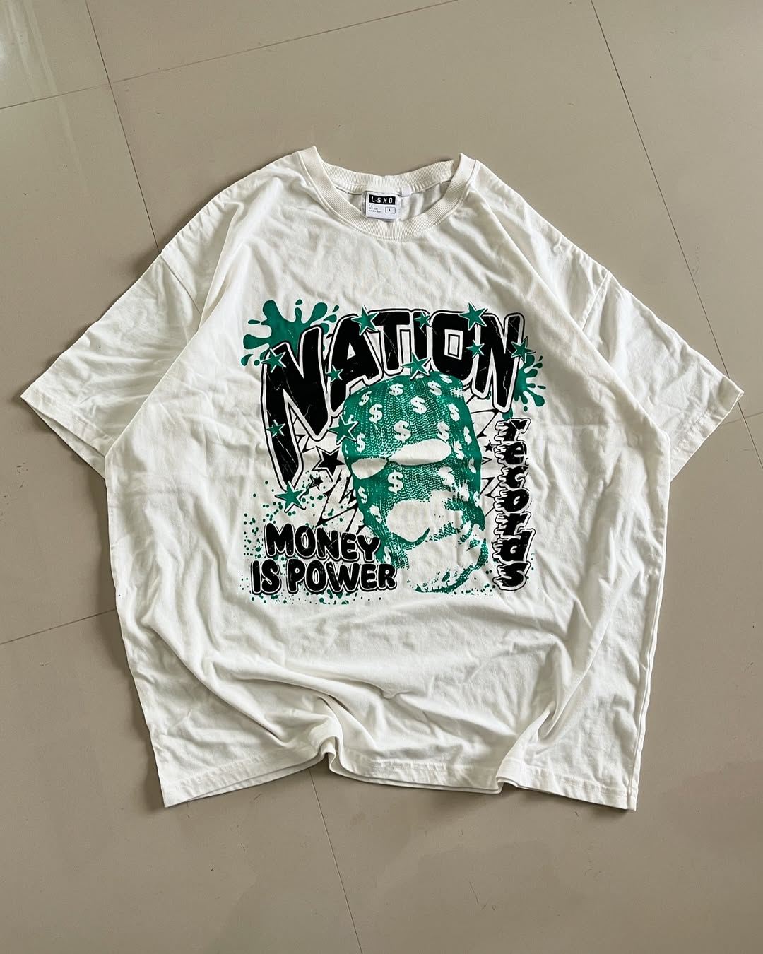 Yellowish oversized graphic tee featuring a teal balaclava mask with dollar signs and bold “NATION” and “MONEY IS POWER” text