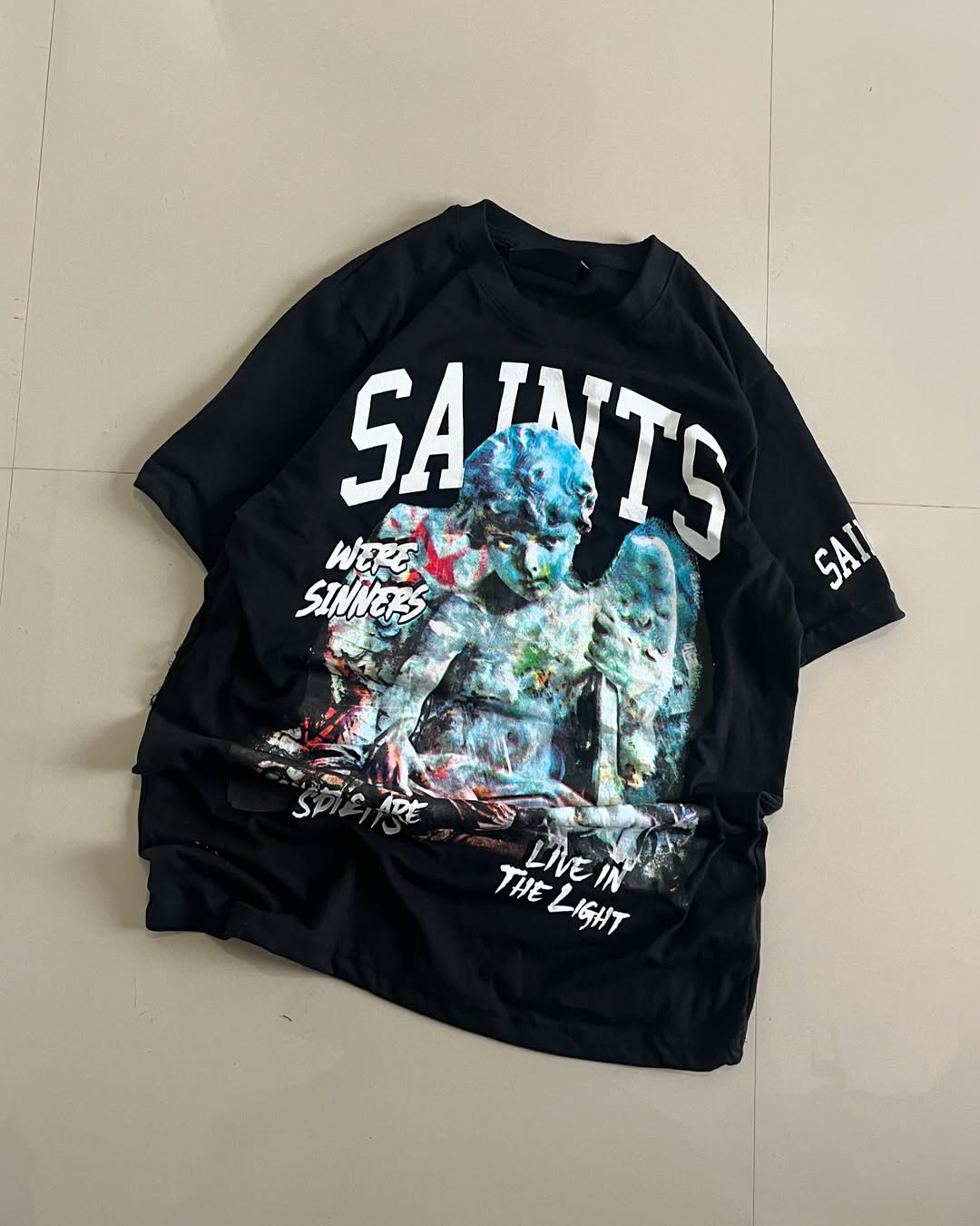 Black oversized t-shirt with colorful angel sculpture print and “SAINTS” text – streetwear by Junk Fits