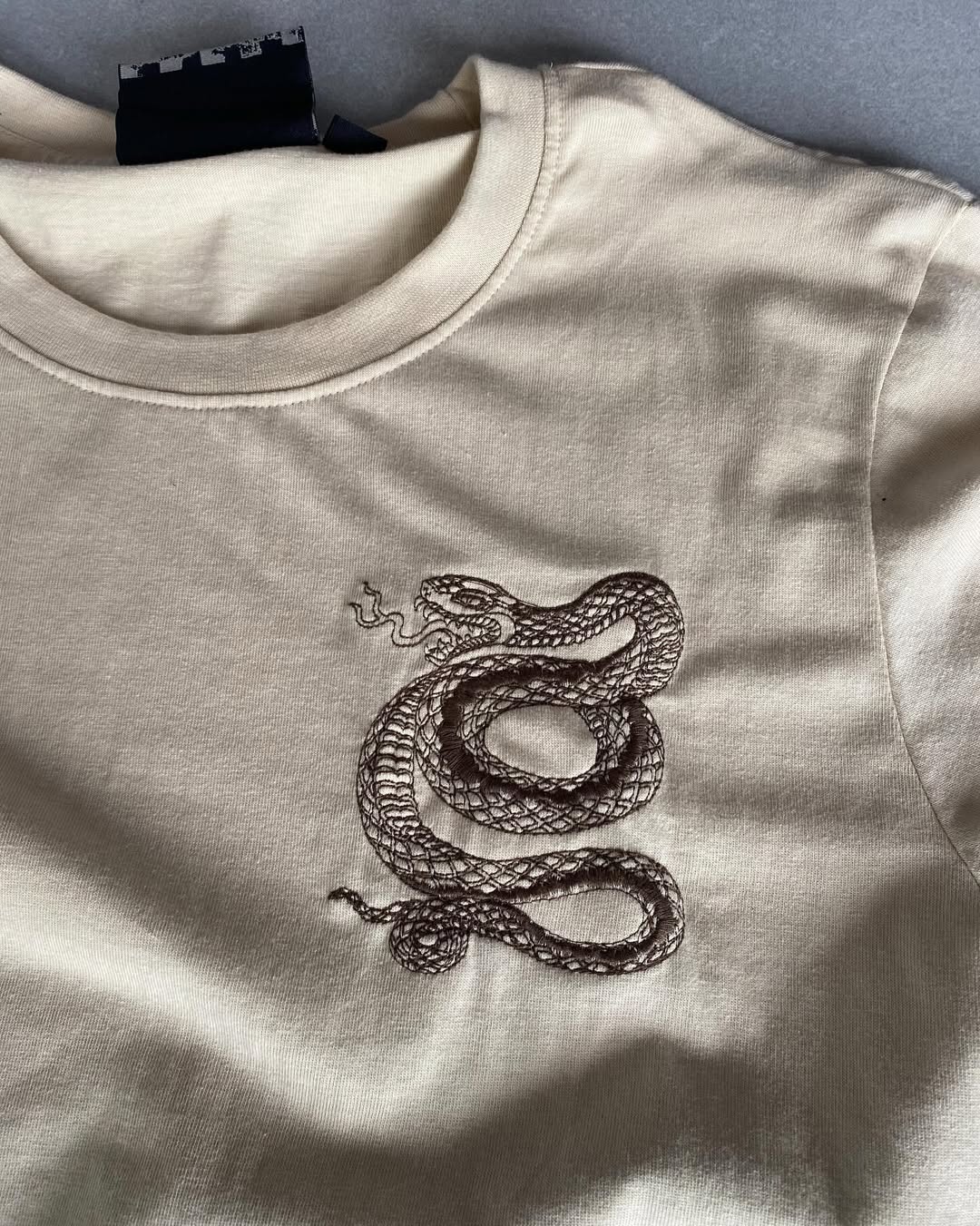 Front view of JunkFits cream t-shirt with minimal design and sleeve patch detail