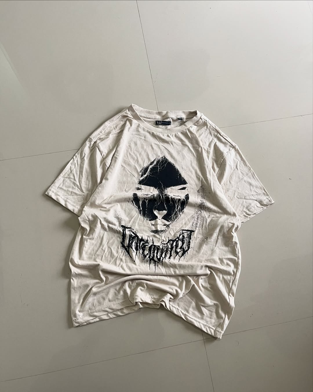 Beige graphic t-shirt featuring eerie monochrome face print and cracked logo

