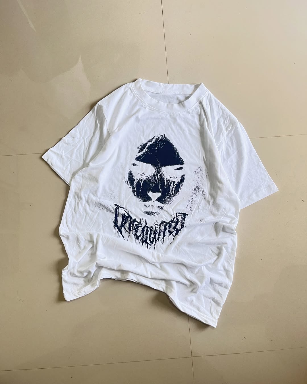 White oversized graphic tee with abstract dark face print and gothic lettering

