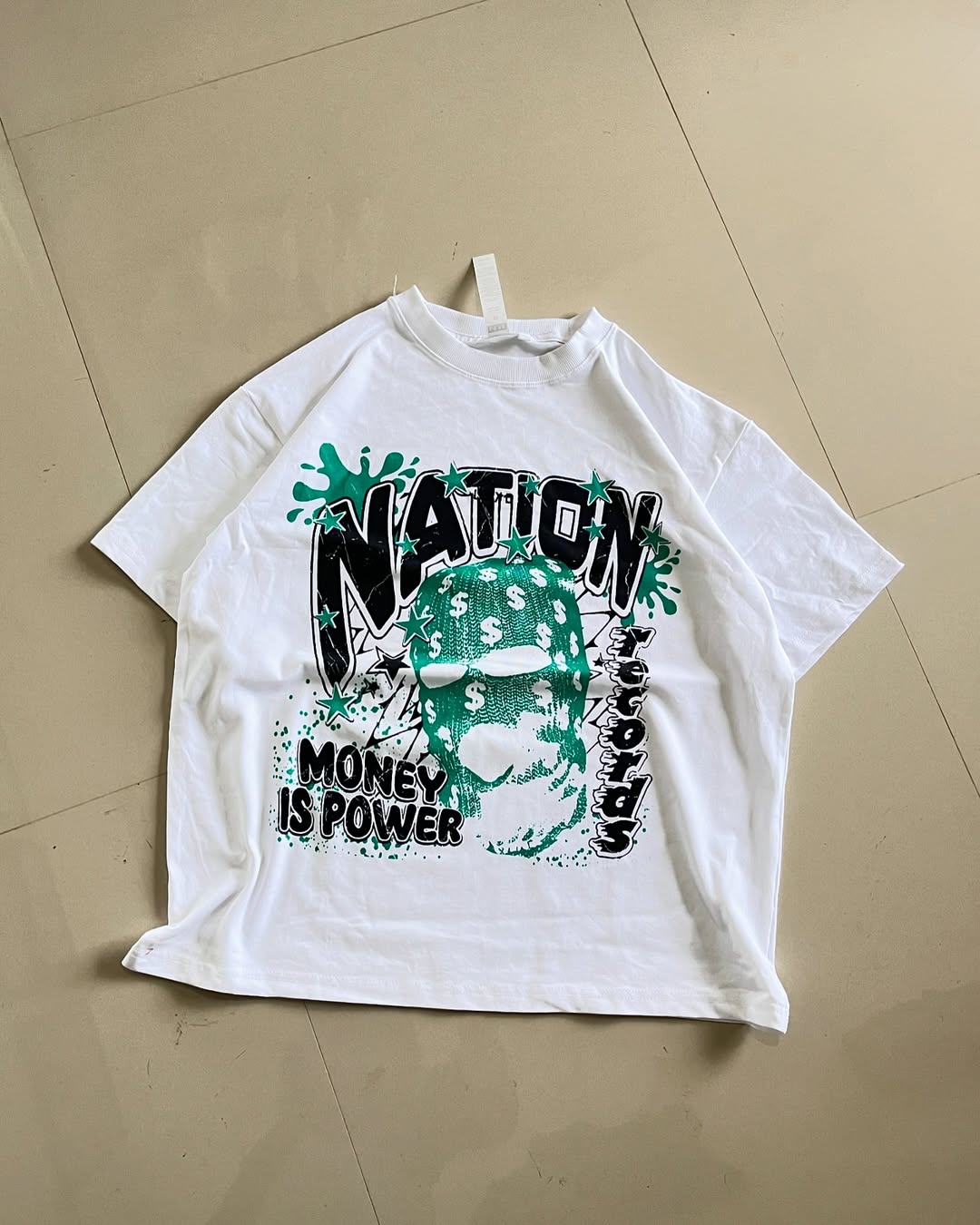 White oversized graphic tee featuring a teal balaclava mask with dollar signs and bold “NATION” and “MONEY IS POWER” text


