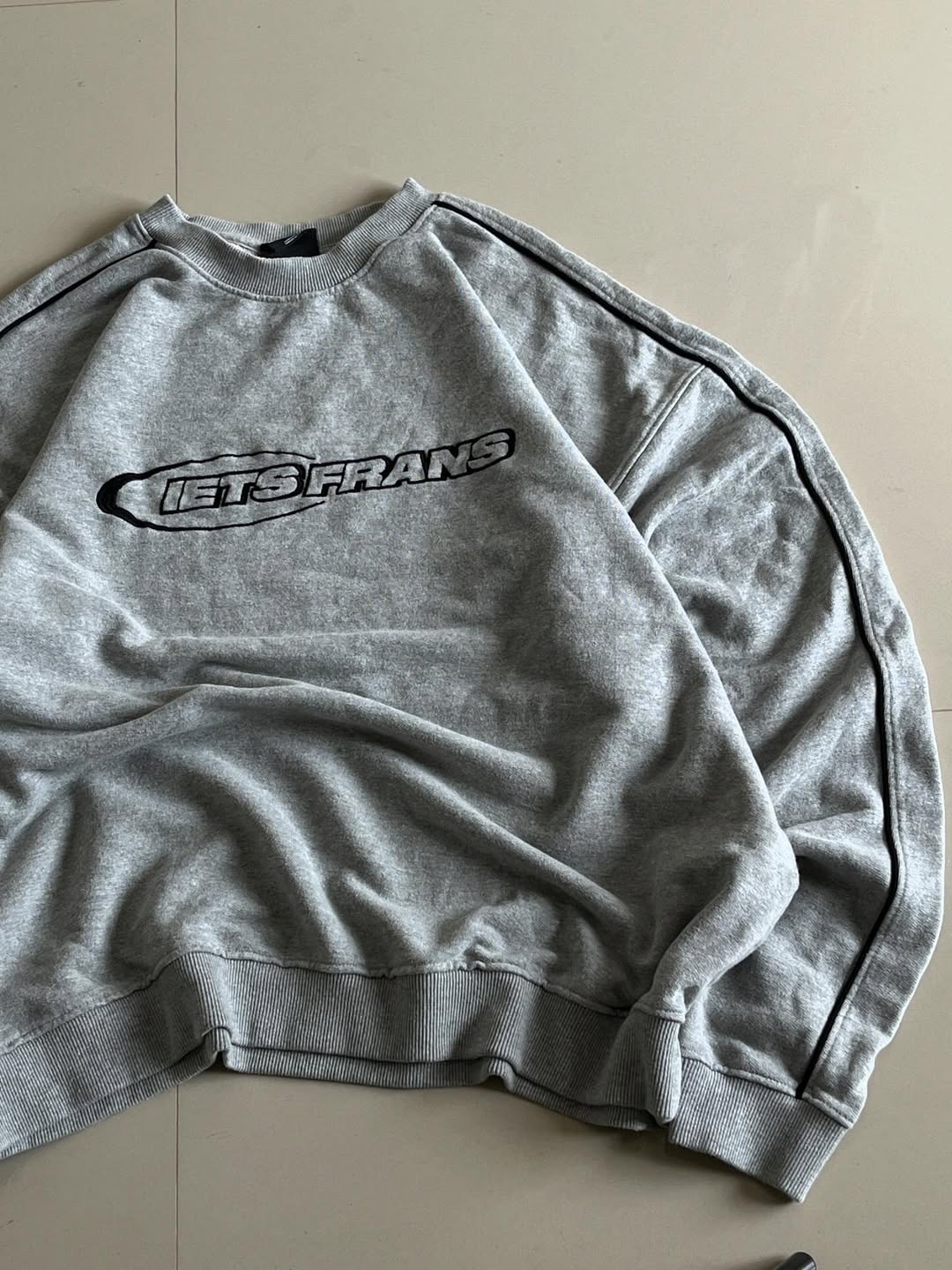 JUNKFITS grey sweatshirt closeup view showing clean panel design and black sleeve piping.