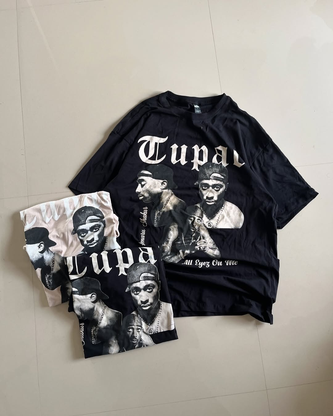 Main image of Tupac graphic t-shirt in black laid flat with beige and white color options beside it


